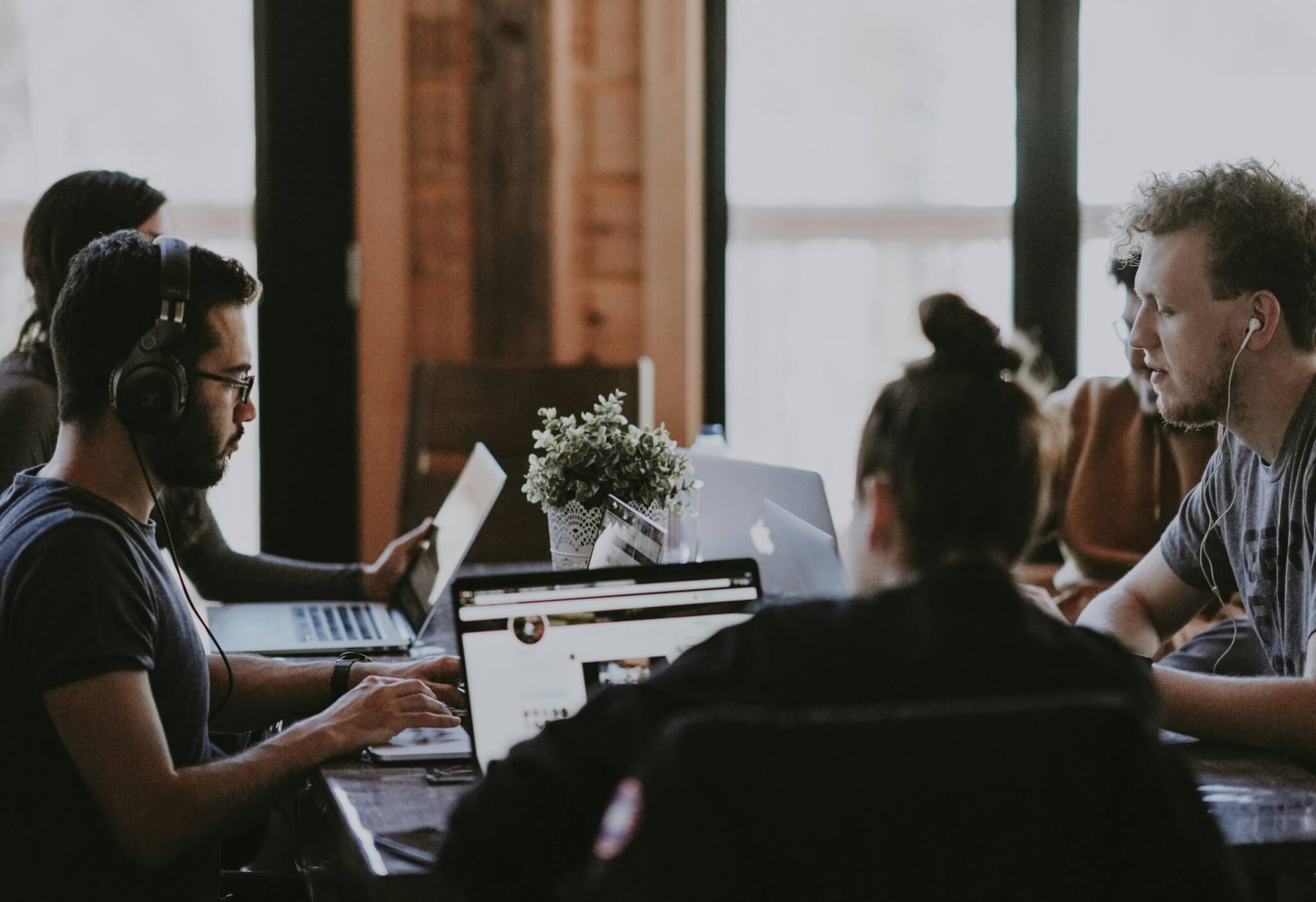 A group of five colleagues sit around a table together, they all have laptops in front of them.